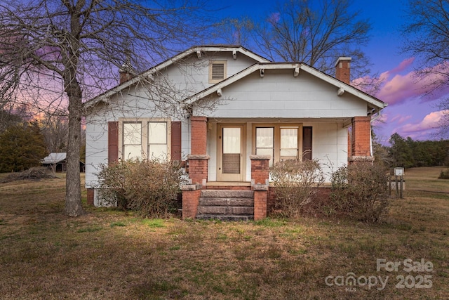 bungalow featuring a yard, brick siding, and a chimney