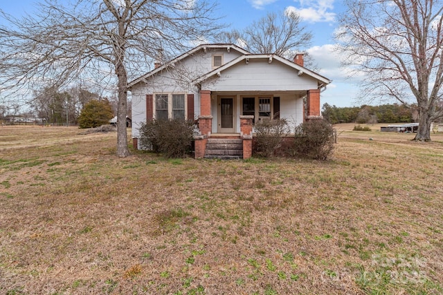 bungalow-style home featuring a porch, a chimney, and a front lawn