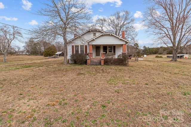 bungalow with a front yard, brick siding, covered porch, and a chimney