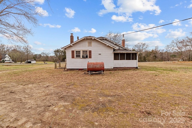 view of side of home with a lawn, a chimney, and a sunroom