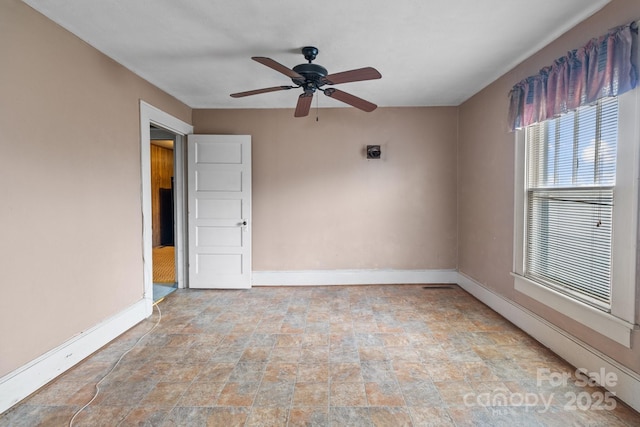 empty room with stone finish flooring, baseboards, and a ceiling fan