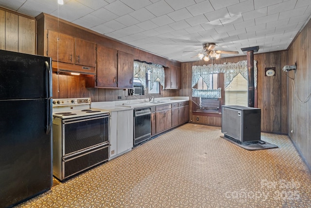 kitchen with wooden walls, under cabinet range hood, light countertops, a wood stove, and black appliances