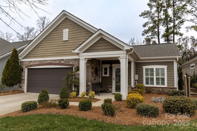 view of front of house with roof with shingles, a porch, concrete driveway, a garage, and stone siding