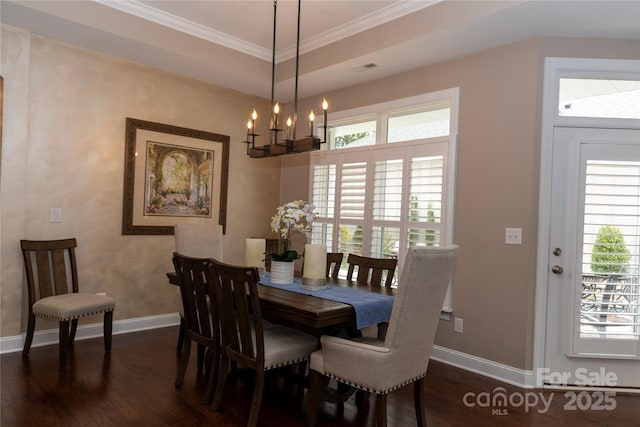 dining area with a notable chandelier, a raised ceiling, dark wood-type flooring, ornamental molding, and baseboards