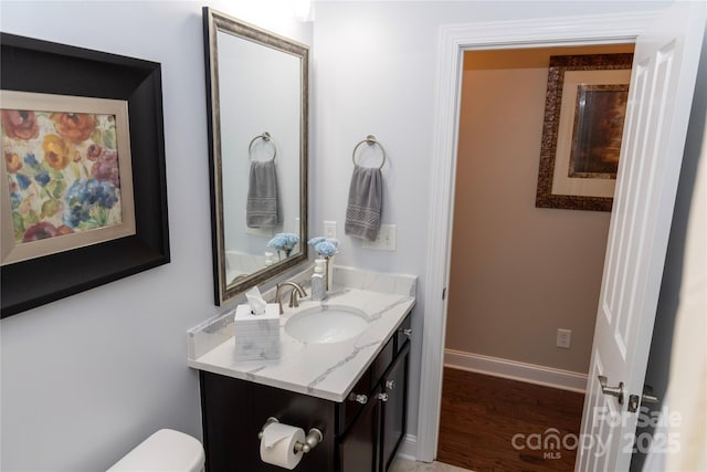 bathroom featuring toilet, baseboards, wood finished floors, and vanity