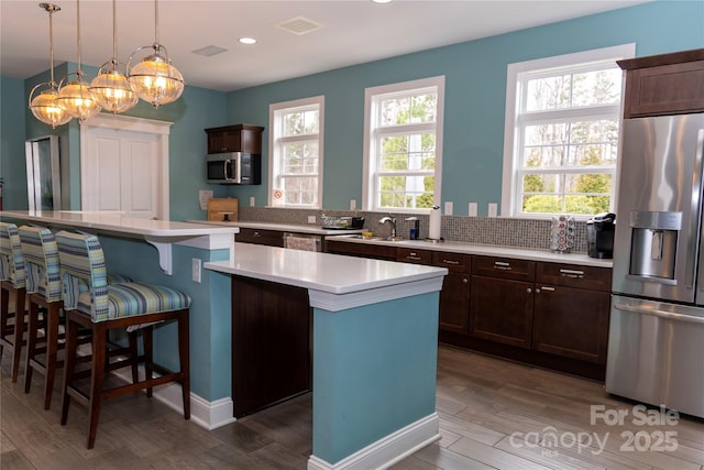 kitchen with dark wood-style floors, a center island, stainless steel appliances, light countertops, and a kitchen bar