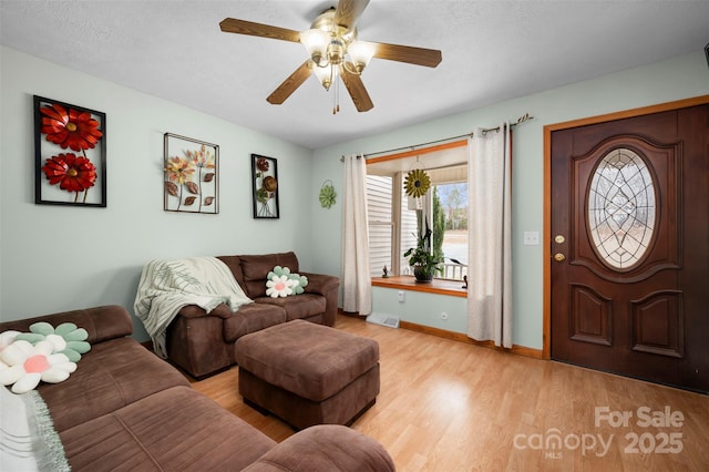 living room with a textured ceiling, light wood finished floors, visible vents, and baseboards