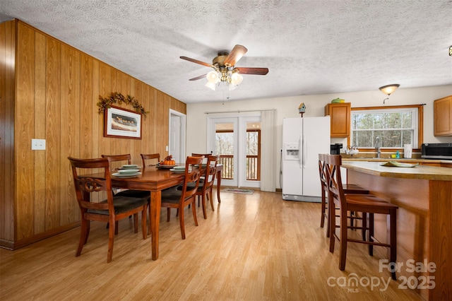 dining space with a textured ceiling, ceiling fan, light wood finished floors, and wood walls