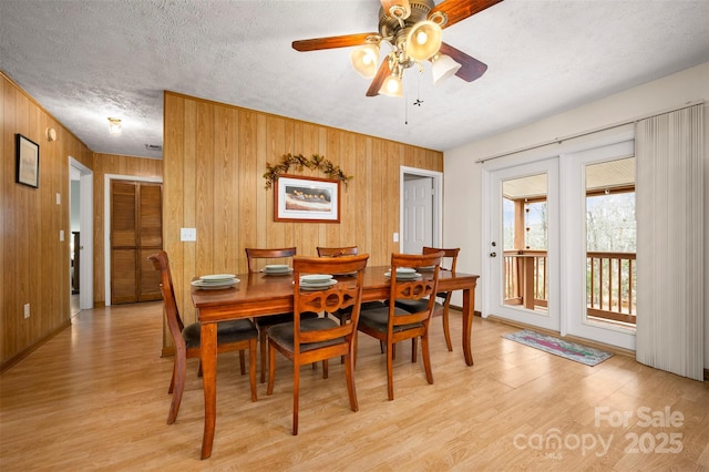 dining space featuring light wood-style floors, wood walls, a textured ceiling, and a ceiling fan