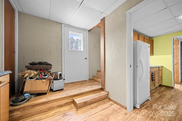 foyer entrance with light wood finished floors, stairway, a drop ceiling, and concrete block wall