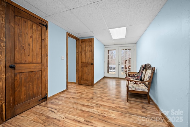 sitting room featuring light wood-style floors, french doors, a drop ceiling, and baseboards