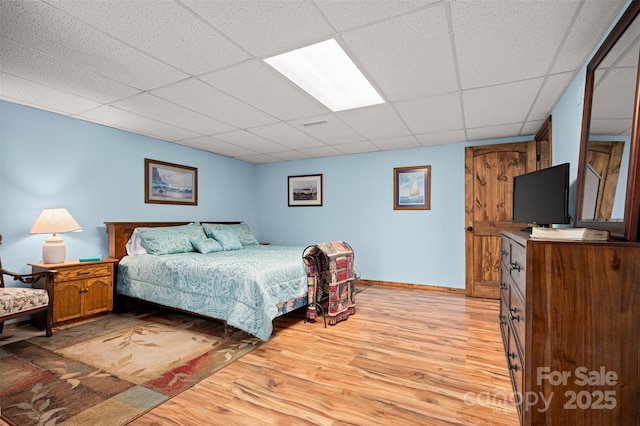 bedroom with light wood-type flooring, a paneled ceiling, and baseboards