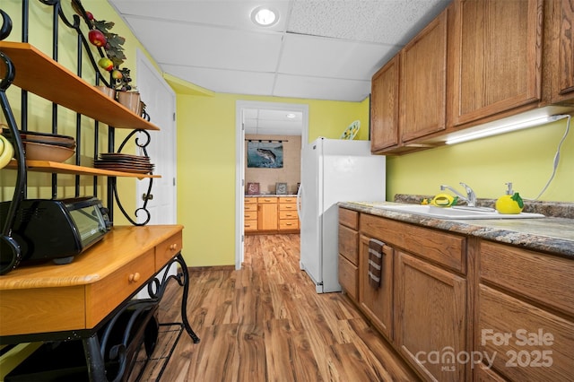 kitchen featuring brown cabinets, open shelves, freestanding refrigerator, wood finished floors, and a drop ceiling