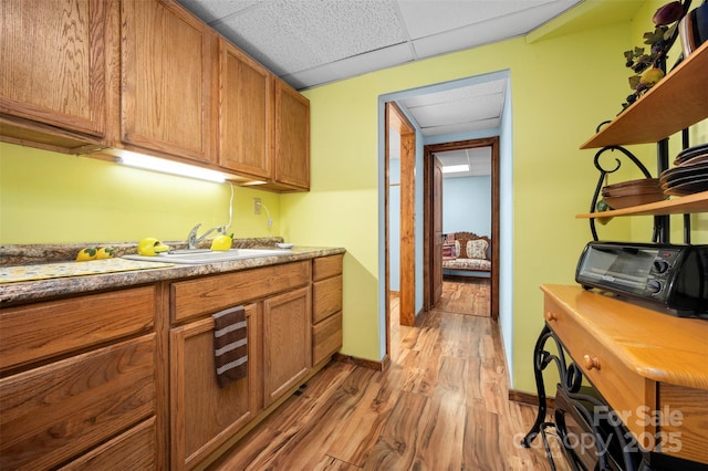 kitchen featuring light wood finished floors, a drop ceiling, brown cabinets, open shelves, and a sink