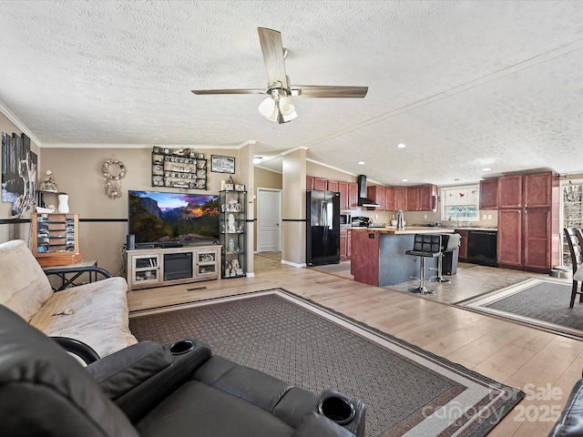 living room with ceiling fan, a textured ceiling, light wood-style floors, vaulted ceiling, and crown molding