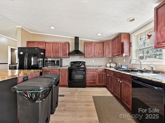 kitchen featuring light wood finished floors, vaulted ceiling, a sink, wall chimney range hood, and black appliances