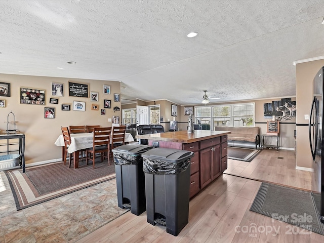 kitchen with a kitchen island, freestanding refrigerator, light wood-type flooring, and vaulted ceiling