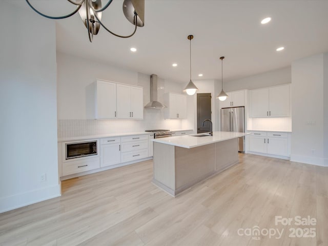 kitchen with a center island with sink, decorative backsplash, appliances with stainless steel finishes, wall chimney range hood, and a sink