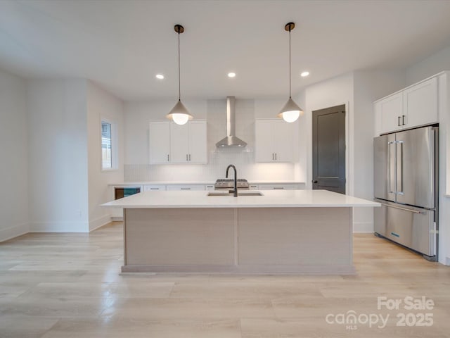 kitchen with light countertops, a kitchen island with sink, white cabinets, high quality fridge, and wall chimney range hood