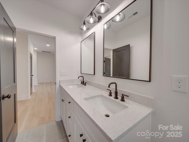 full bath with double vanity, visible vents, a sink, and wood finished floors