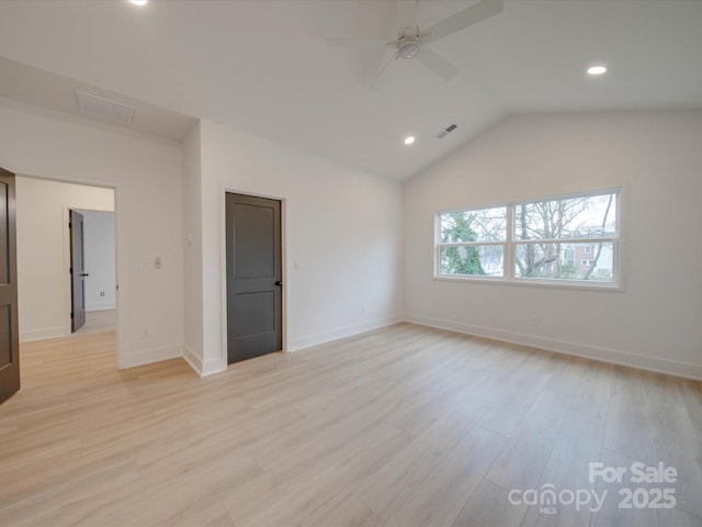 spare room with vaulted ceiling, light wood-type flooring, visible vents, and baseboards