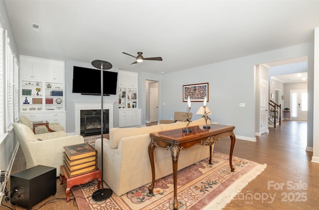 living area featuring light wood-type flooring, visible vents, a glass covered fireplace, baseboards, and stairs