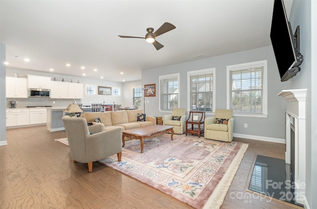 living room featuring baseboards, light wood-style flooring, a fireplace with flush hearth, recessed lighting, and ceiling fan