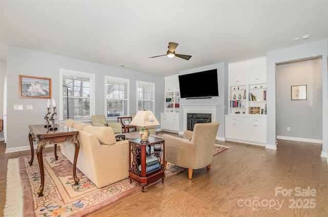 living area featuring a glass covered fireplace, ceiling fan, baseboards, and light wood-style floors