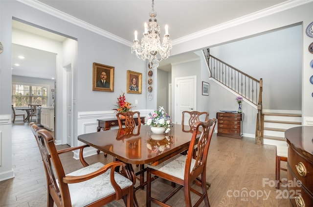 dining area featuring ornamental molding, wood finished floors, wainscoting, a chandelier, and stairs