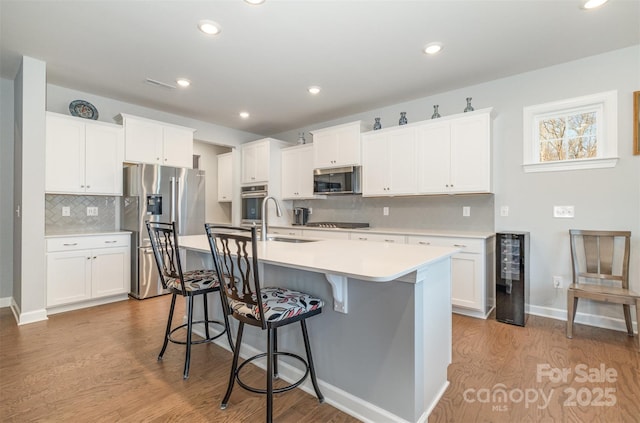 kitchen with wood finished floors, beverage cooler, a center island with sink, a sink, and appliances with stainless steel finishes