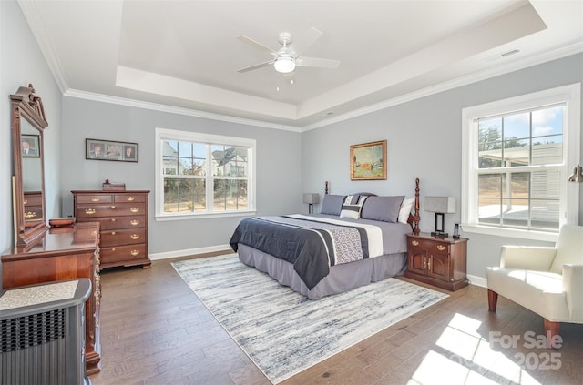 bedroom with baseboards, crown molding, a tray ceiling, and wood finished floors