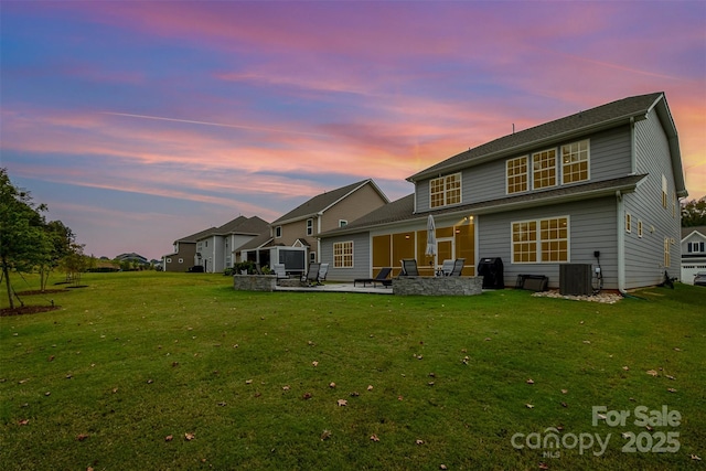 back of property at dusk featuring central air condition unit, a lawn, and a patio