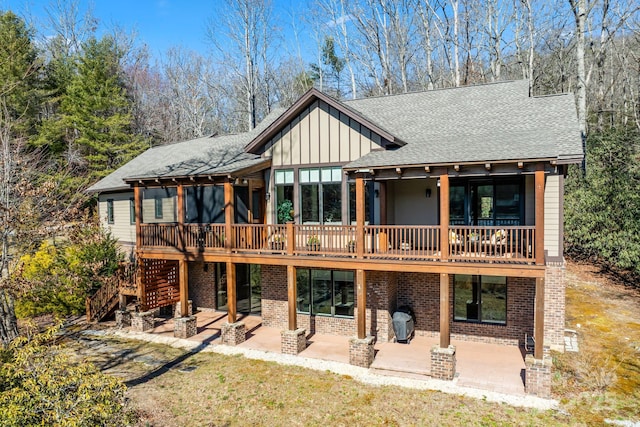 rear view of property with brick siding, board and batten siding, a shingled roof, and a patio area