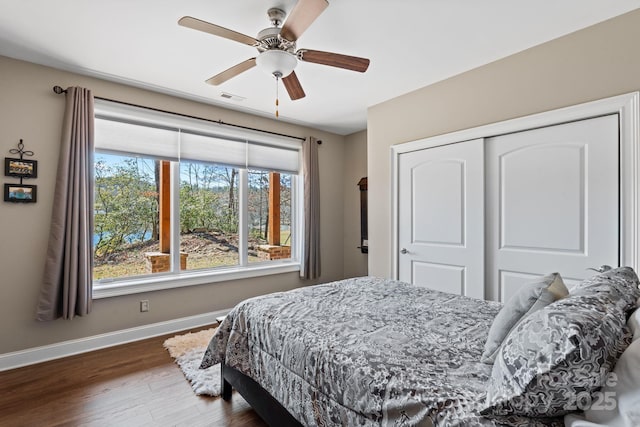 bedroom with visible vents, wood finished floors, a closet, baseboards, and ceiling fan