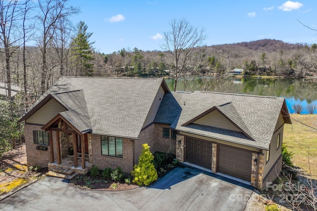 view of front of home featuring a forest view, a shingled roof, a garage, a water view, and aphalt driveway