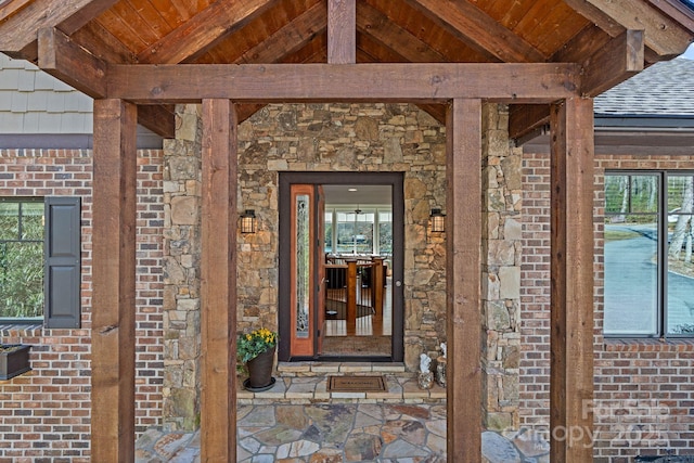 entrance to property with brick siding, stone siding, and a shingled roof