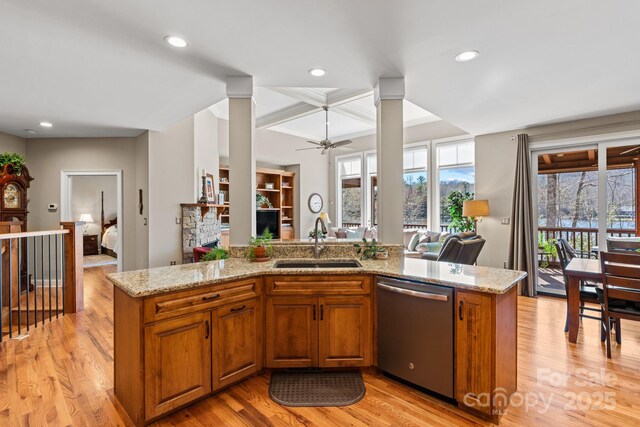 kitchen featuring brown cabinetry, light stone countertops, a sink, light wood-style floors, and stainless steel dishwasher