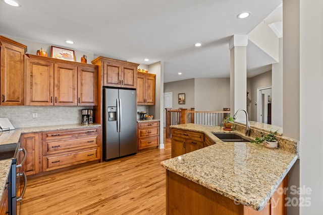 kitchen featuring a sink, tasteful backsplash, light wood-style floors, appliances with stainless steel finishes, and brown cabinetry