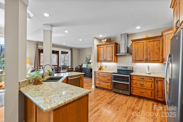 kitchen with brown cabinets, a sink, appliances with stainless steel finishes, wall chimney exhaust hood, and decorative backsplash