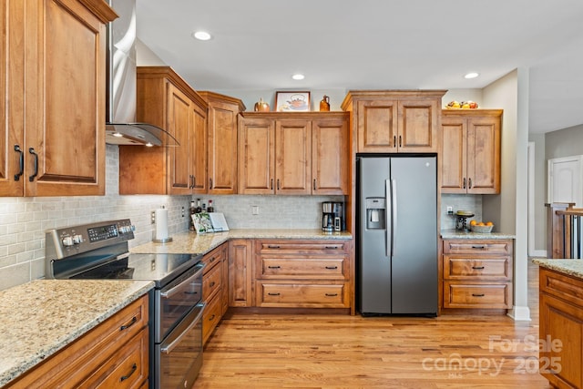 kitchen with brown cabinetry, light wood-style flooring, stainless steel appliances, and wall chimney exhaust hood