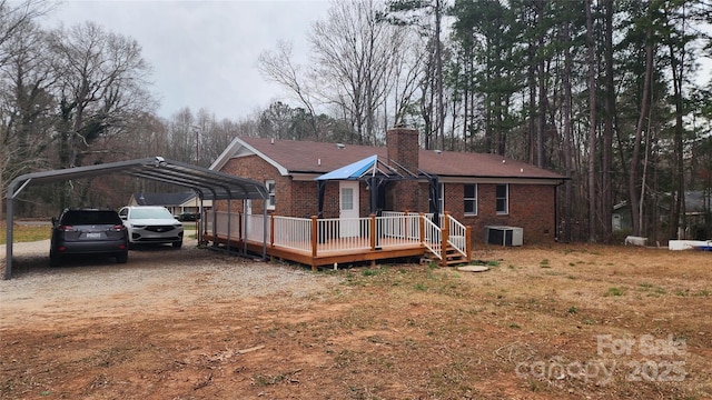 back of property featuring a wooden deck, central AC, a chimney, a carport, and brick siding