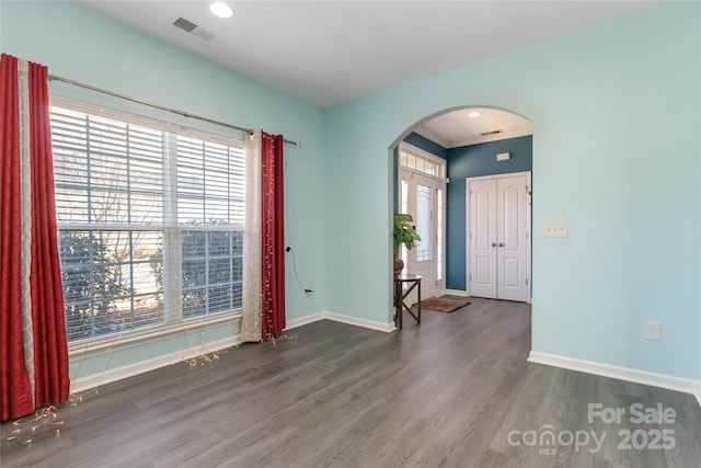 unfurnished room featuring wood finished floors, visible vents, arched walkways, and baseboards