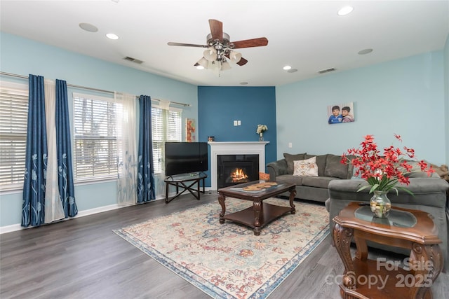 living area featuring visible vents, baseboards, a lit fireplace, and wood finished floors