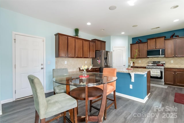 kitchen with light stone countertops, dark wood-type flooring, appliances with stainless steel finishes, and a breakfast bar area