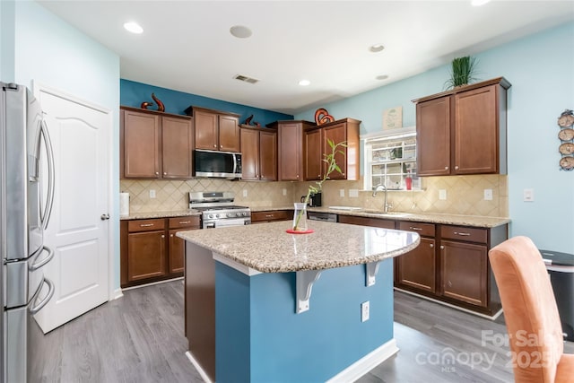 kitchen featuring light stone counters, wood finished floors, visible vents, a kitchen island, and appliances with stainless steel finishes