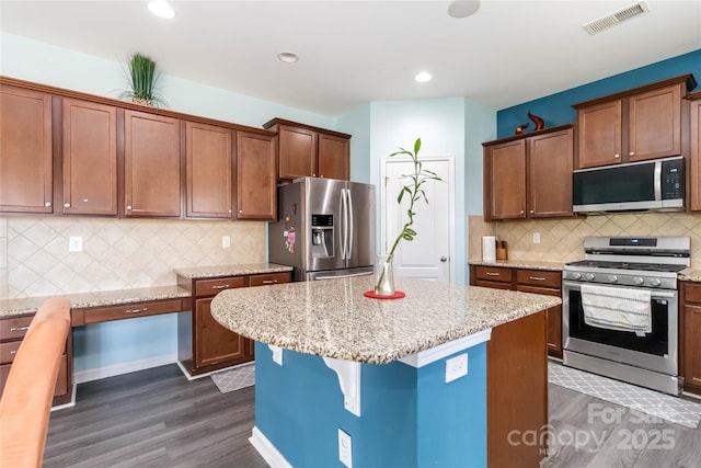 kitchen with visible vents, light stone countertops, a breakfast bar area, appliances with stainless steel finishes, and dark wood-style floors