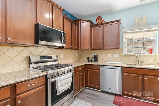 kitchen with tasteful backsplash, light stone countertops, light wood-type flooring, stainless steel appliances, and a sink