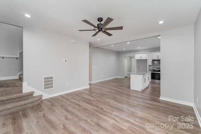 unfurnished living room featuring ceiling fan, visible vents, light wood finished floors, and stairway