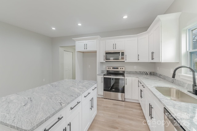 kitchen with white cabinets, appliances with stainless steel finishes, a sink, light wood finished floors, and recessed lighting