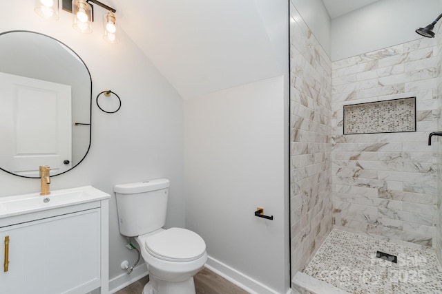 bathroom featuring vanity, wood finished floors, toilet, baseboards, and a tile shower